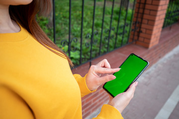 Young girl in a yellow sweater holds a phone with a green screen and scrolls