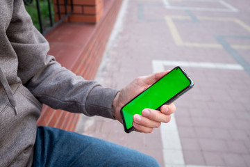 Young man in gray sweatshirt holds a phone with a green screen