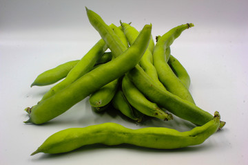 pile of fresh green broad beans in their shells isolated on a white background