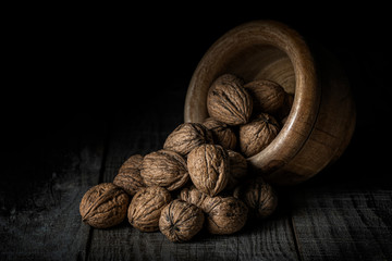 nuts spilled from a wooden bowl on a black background