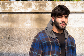 Obraz premium Young handsome bearded Indian hipster man thinking in the streets