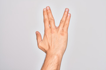 Hand of caucasian young man showing fingers over isolated white background greeting doing Vulcan salute, showing back of the hand and fingers, freak culture