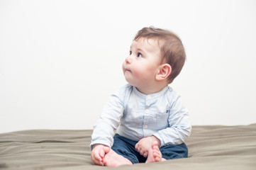Naklejka premium Profile view of a cute baby boy sitting in bed with a peaceful expression.