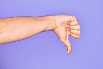 Hand of caucasian young man showing fingers over isolated purple background doing thumbs down rejection gesture, disapproval dislike and negative sign