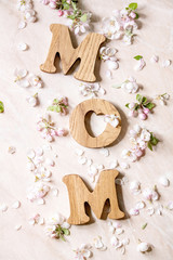 Obraz na płótnie Canvas Mother's day greeting card. Wooden letters MOM with spring apple flowers and petals over pink marble background. Flat lay, space