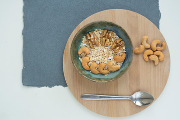 Oatmeal with cashews and walnuts on a wooden tray and blue and white background. Healthy breakfast