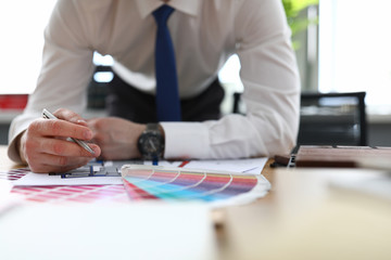 Close-up of man in stylish suit holding silver pen. Male person in office. Creative designer and architect. Colourful samples palette. House renovation and new interior concept