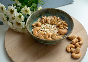 Oatmeal with cashews and walnuts and white flowers on a wooden tray and blue and white background. Healthy breakfast