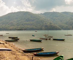 Fototapeta na wymiar Wooden boats idle on the banks of the Phewa lake in the Himalayan city of Pokhara 