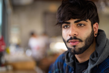 Obraz premium Young handsome bearded Indian hipster man at the coffee shop