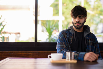 Fototapeta na wymiar Young handsome bearded Indian hipster man at the coffee shop