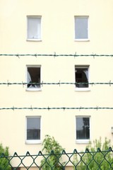 Rows of barbed wire against a abandoned residential building with broken windows background. Ghost...
