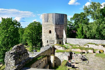 Cesis, Latvia - Cesis castle, tower and ruined stone walls on a background of green trees and blue sky with clouds, in the summer in the daytime.