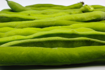 row of fresh green broad beans in their shells isolated on a white background