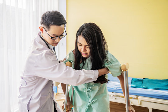 Front View Of Asian Male Doctor Helping Female Patient To Walk Out The Hospital Bed, Medicine And Health Care Concept, Selective Focus Point