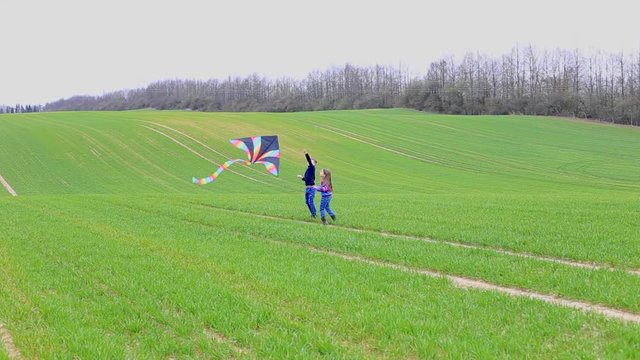 Children launch a kite in a field in spring. Boy and girl run across the field with a kite