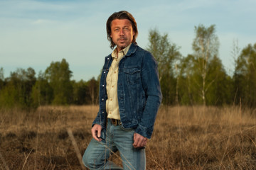 Naklejka na ściany i meble Man in jeans jacket and shirt in nature reserve at sunrise during spring.