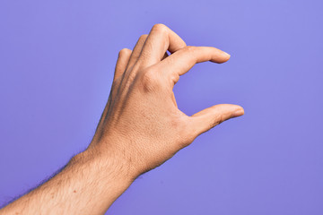 Hand of caucasian young man showing fingers over isolated purple background picking and taking invisible thing, holding object with fingers showing space