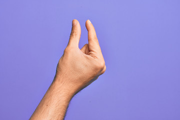 Hand of caucasian young man showing fingers over isolated purple background picking and taking invisible thing, holding object with fingers showing space