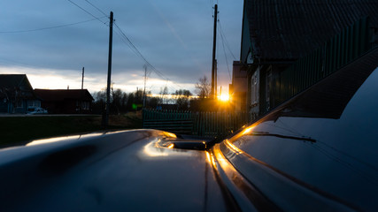 evening in the village. spring. reflections of the setting sun on the car.
