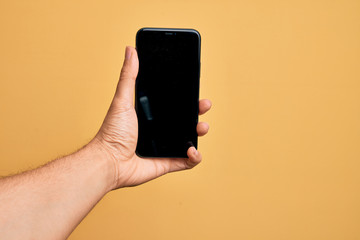 Fototapeta na wymiar Hand of caucasian young man holding smartphone showing screen over isolated yellow background
