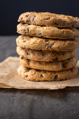 Close-up of chocolate chip cookies in stack, on paper and dark tablecloth, vertical, with copy space