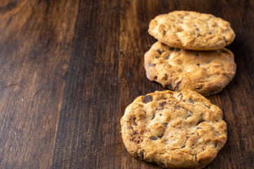 Top view of three chocolate chip cookies, with selective focus, on dark wooden table, horizontal, with copy space