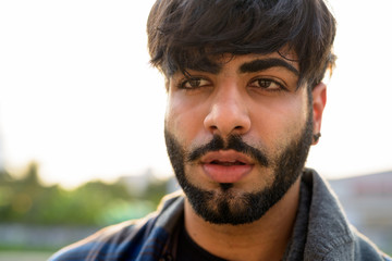Face of young handsome bearded Indian hipster man thinking in urban streets