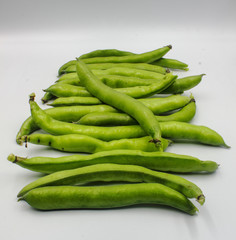 row of fresh green broad beans in their shells isolated on a white background