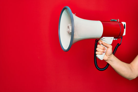 Beautiful hand of man holding megaphone over isolated red background
