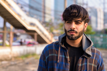 Young handsome bearded Indian hipster man in the city streets outdoors