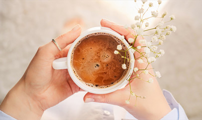 Cup of fragrant morning coffee in a cozy atmosphere of home. Close-up of holding hot ceramic white coffee cup. Good morning.