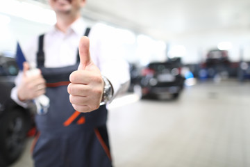 Close-up of person showing thumbs up. Good job and well done symbol. Copy space in right side. Mechanic in uniform posing in garage. Repair service station and handyman concept