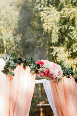 Wedding arch in the forest, in the fresh air, on the pier. Arch, decorated with beautiful fresh flowers and fabric. White, green & pink color. Wedding arch of real flowers.