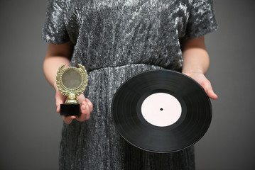 Music award ceremony concept. A singer with golden award trophy and vinyl record in hands on gray...