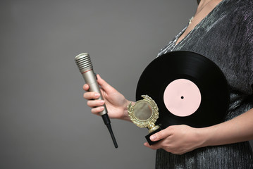 Music award ceremony concept. A singer with golden award trophy and vinyl record in hands on gray...
