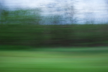 Defocused background of window view of moving car. Blurry image of grass, sky and trees
