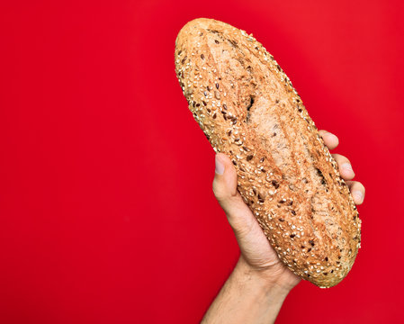 Beautiful hand of man holding wholemeal integral bread with cereals over isolated red background