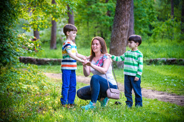 Fototapeta premium Young woman mother applying insect repellent to her two son before forest hike beautiful summer day or evening. Protecting children from biting insects at summer. Active leisure with kids