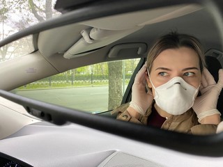 girl in a protective mask looks in the mirror in a car. During quarantine- coronavirus.  Covid-19.