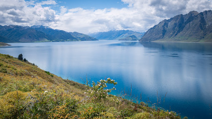 Naklejka na ściany i meble Scenic alpine lake surrounded by mountains shot on sunny day. Location is lake Hawea, New Zealand.