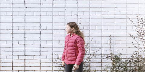 Happy girl rejoices spring. Young child playing outside. Banner of Sunny day activity with copyspace. Happy, joyful kid outdoors. Having fun alone. Beautiful landscape with white brick wall.