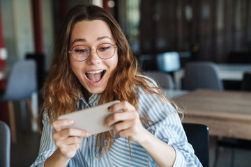 Image of excited woman playing video game on cellphone at classroom