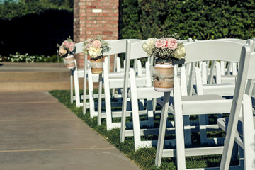 wedding ceremony aisle with white wooden chairs and pink roses in small jars 