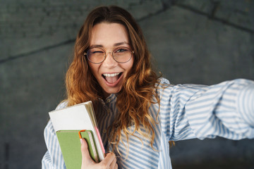 Image of woman winking and holding exercise books while taking selfie