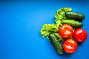 Fresh vegetables on a blue dackground. Cucumbers, tomatoes and lettuce. Healthy eating and vegetarianism concept.