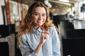 Image of cheerful woman smiling and writing on planner while sitting