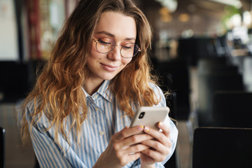 Image of cheerful young woman smiling and typing on cellphone