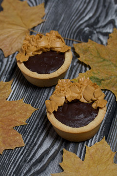 Tartlets with chocolate ganache. On autumn maple leaves. Decorated with oil cream flowers. The cream has a caramel color. On brushed pine boards painted black.