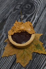 Tartlets with chocolate ganache. On autumn maple leaves. Decorated with oil cream flowers. The cream has a caramel color. On brushed pine boards painted black.